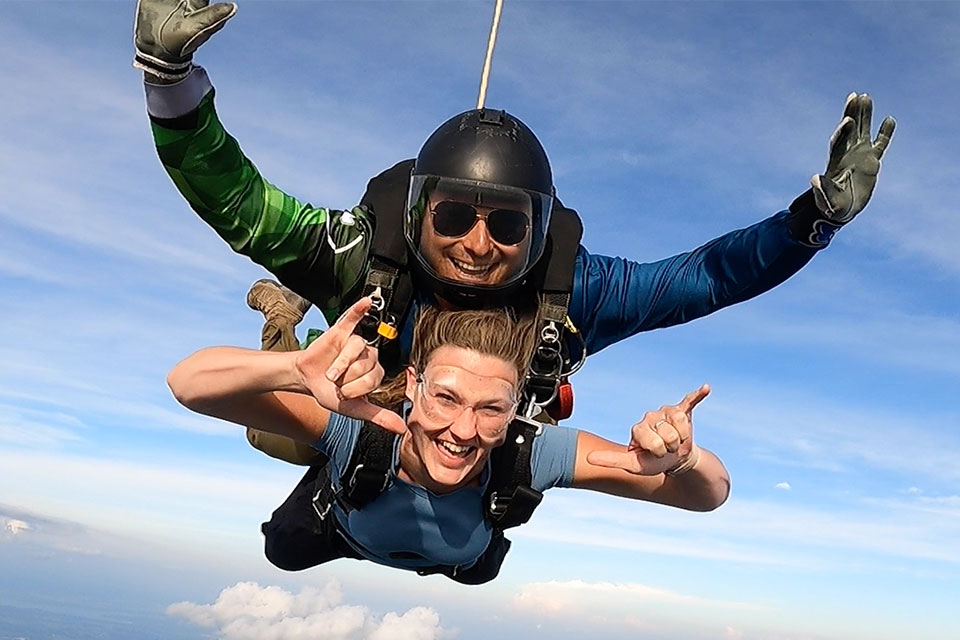 Female tandem skydiving student giving the rock on signal with her hands while in freefall over Parachute Ottawa in Ontario