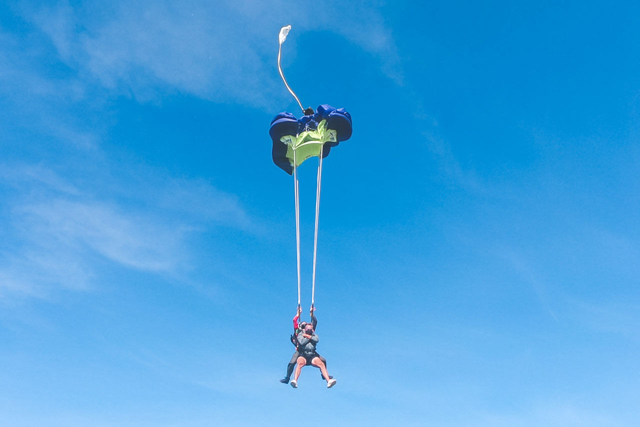Tandem skydiving student and instructor against blue sky preparing for canopy to open