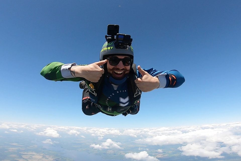 Licensed skydiver with mustache giving two thumbs up while in freefall over Parachute Ottawa in Arnprior, ON