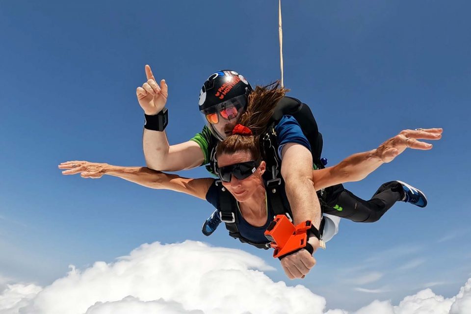 Female tandem skydiving student in freefall with blue sky and puffy white clouds