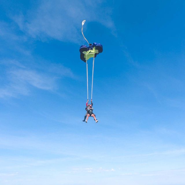 Tandem skydiving student and instructor against blue sky preparing for canopy to open