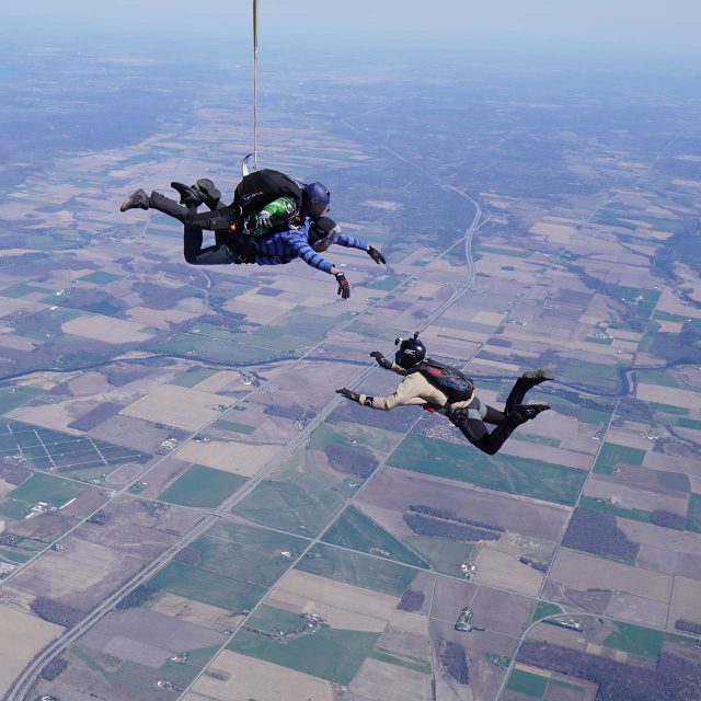 Outside view of a videographer capturing a tandem skydiving student and instructor in freefall