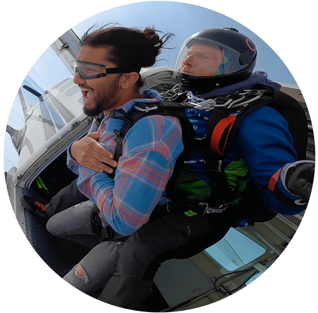 Male tandem skydiving student wearing a blue and red flannel shirt preparing to exit a plane with his skydiving instructor at Parachute Ottawa in Ontario
