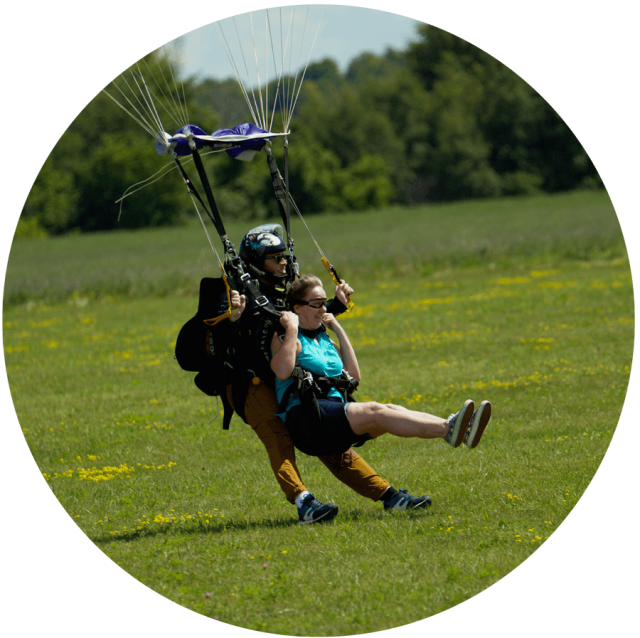 Female tandem skydiving student with legs lifted landing in a grassy field at Parachute Ottawa