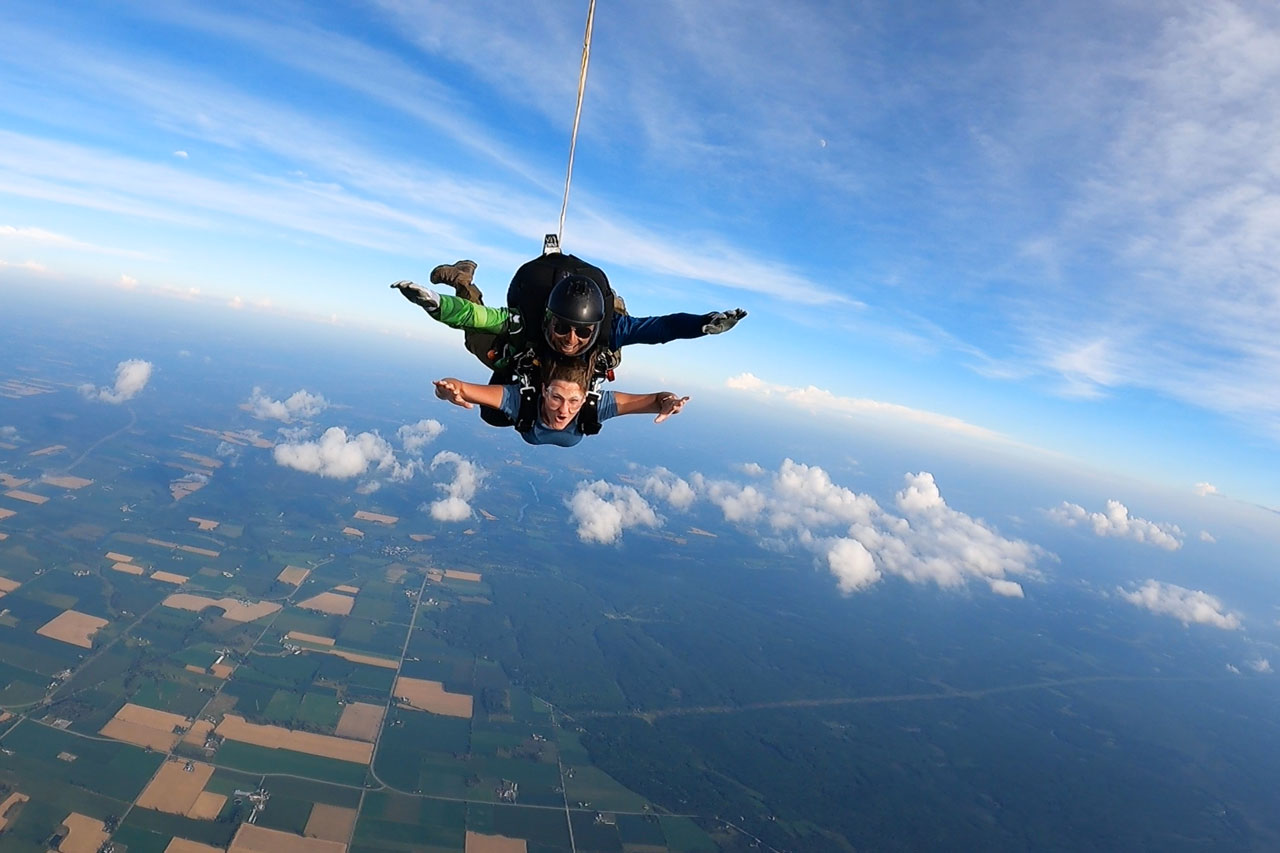Female tandem skydiving student in freefall smiling at the camera