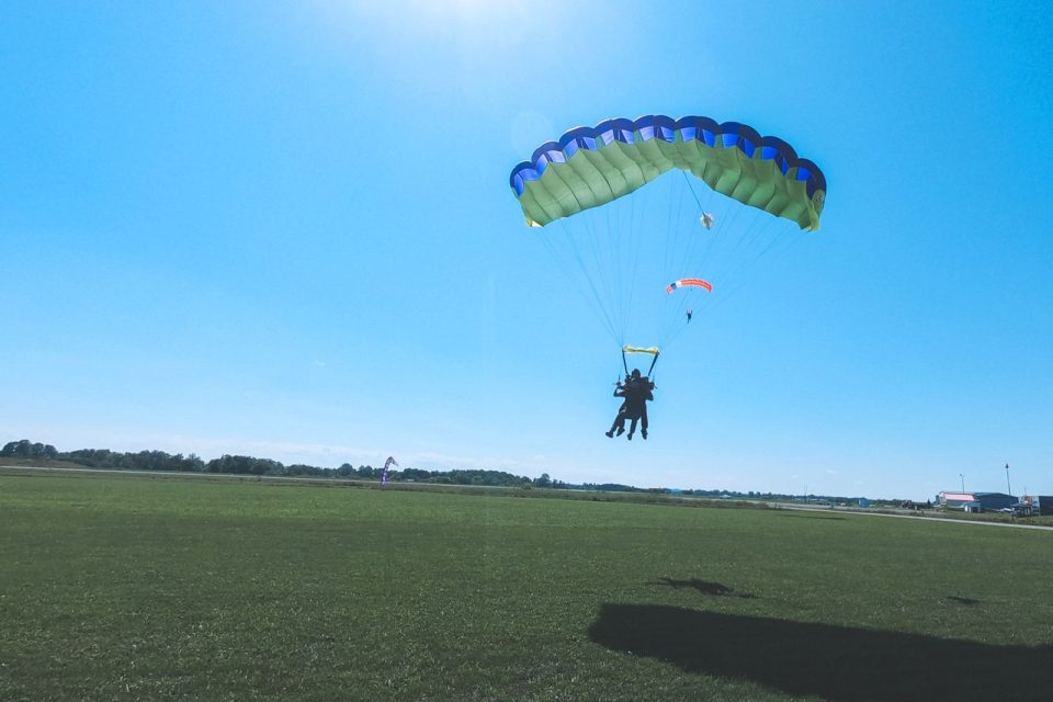 Tandem skydiver and instructor coming in for landing in a large grassy field at Parachute Ottawa skydiving center in Canada