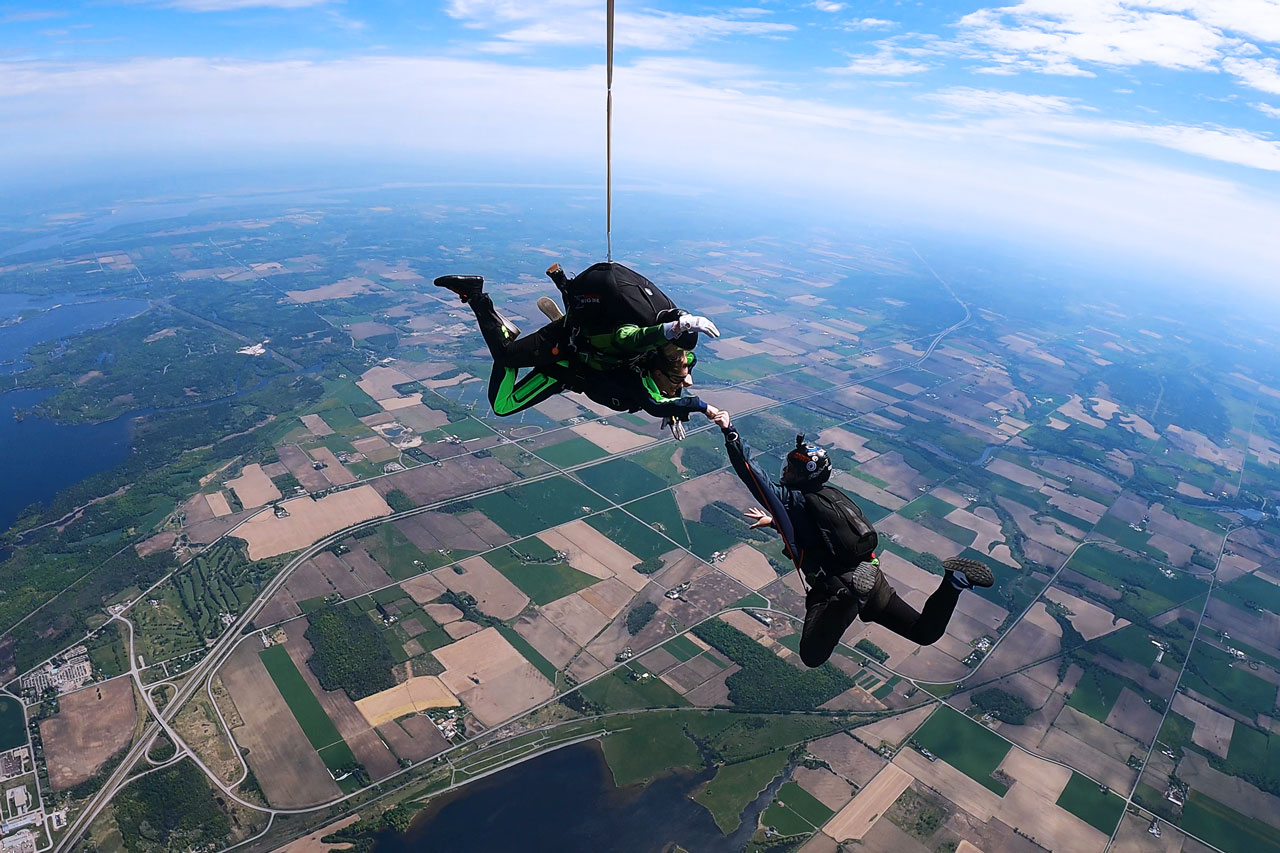 Tandem skydiving student fist bumping a videographer in freefall over Parachute Ottawa in Ontario