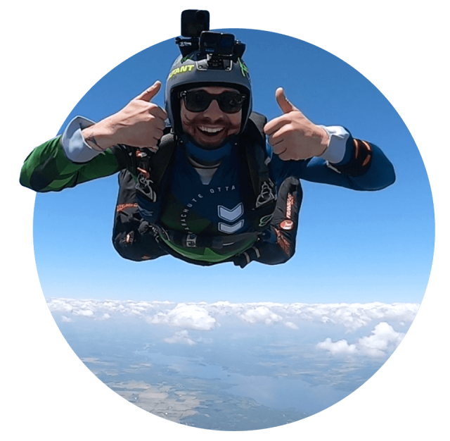 Licensed skydiver with mustache giving two thumbs up while in freefall over Parachute Ottawa in Arnprior, ON